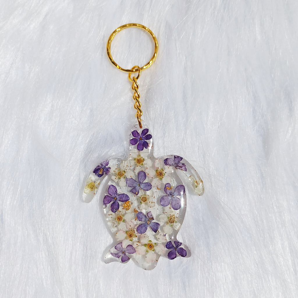 Un porte-clé en forme de tortue, délicatement orné de fleurs de lilas séchées