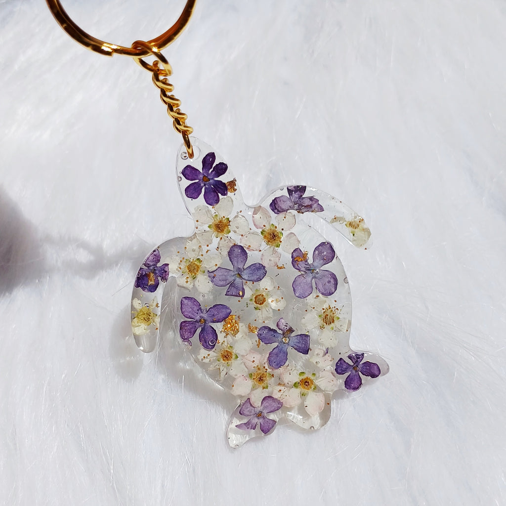 Un porte-clé en forme de tortue, délicatement orné de fleurs de lilas séchées